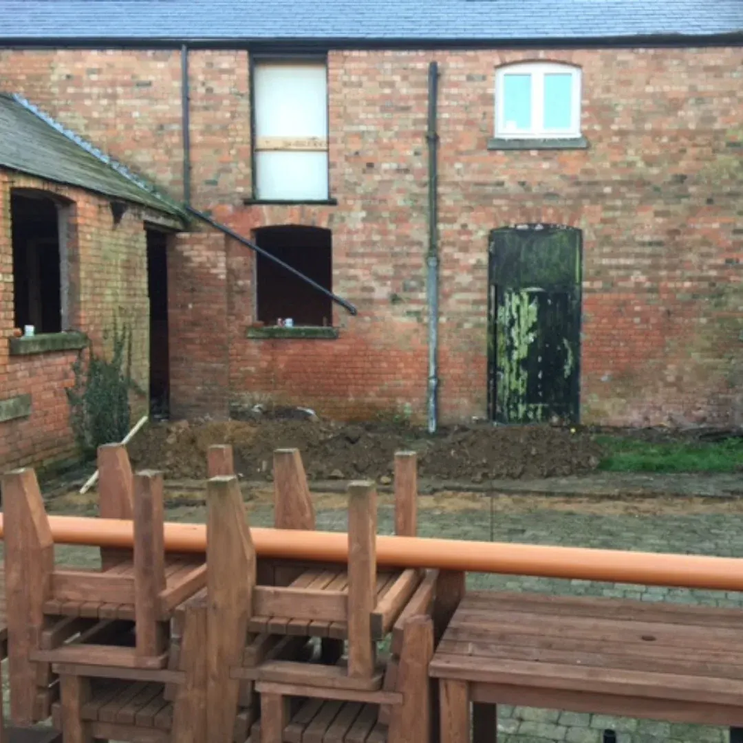 The barns before the conversion: a derelict brick building with broken windows, a weathered door and old benches stacked in the yard