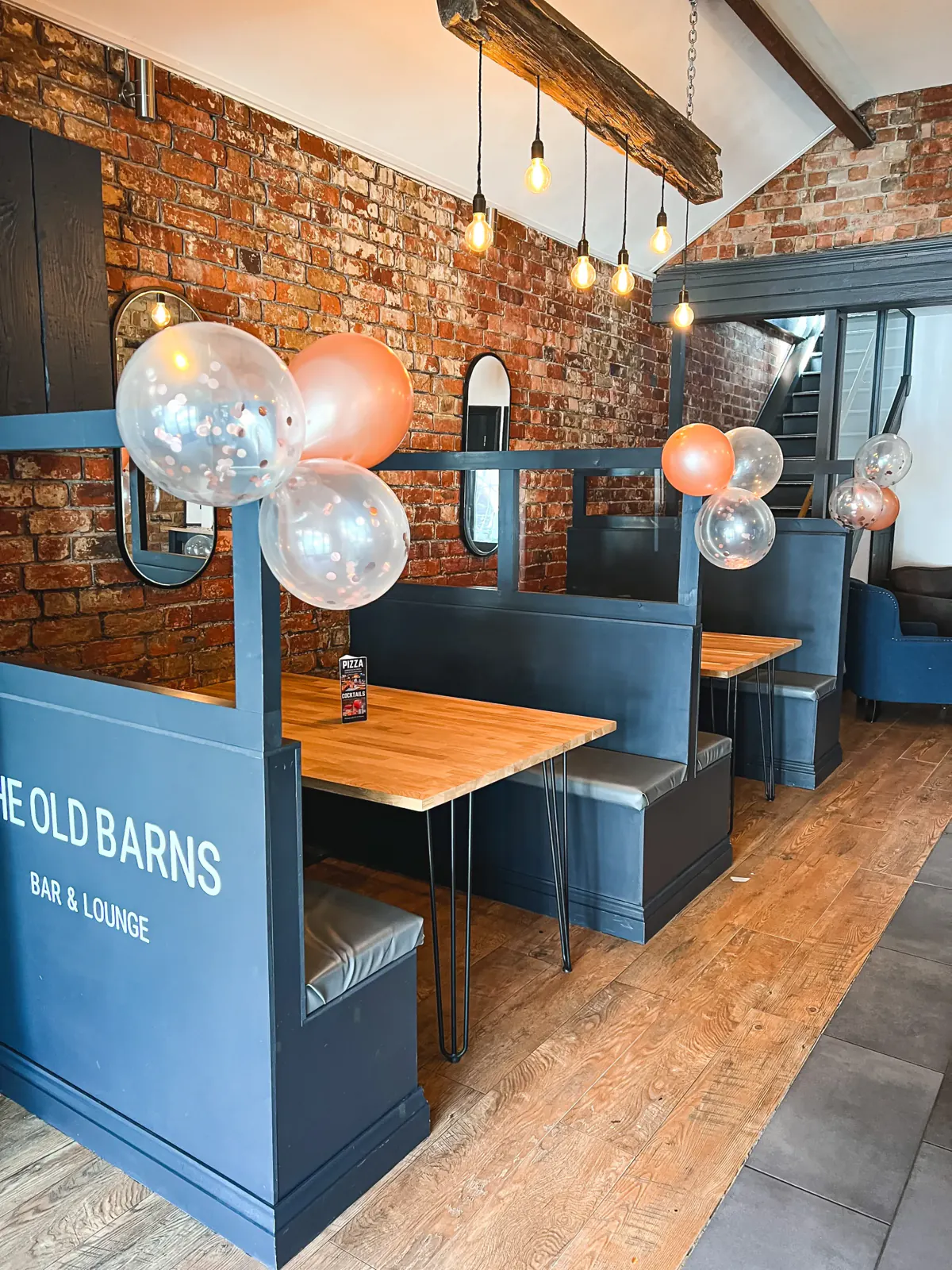 Slate-blue booths decorated with clear and copper balloons, under a timber beam hung with Edison bulbs