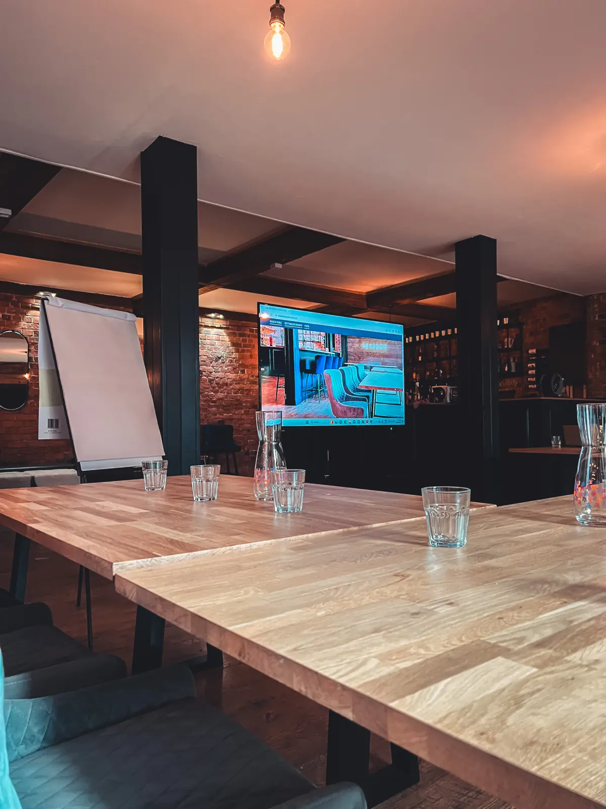 Oak tables laid with glasses and water jugs in front of a wall-mounted screen and a flip chart, ready for a presentation