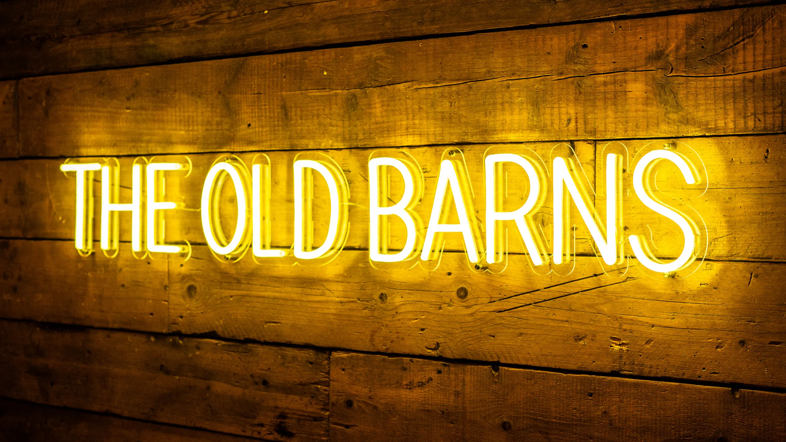 The Old Barns neon sign glowing amber against reclaimed timber boards