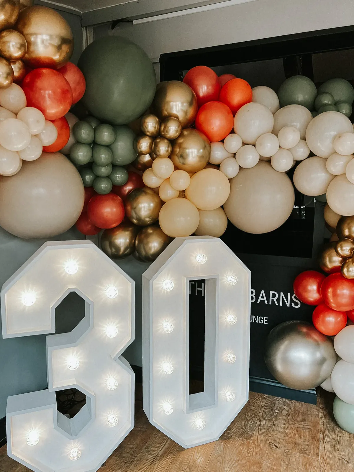 Giant light-up 30 numbers in front of a balloon garland in cream, gold, sage and red